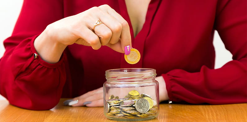 Frau wirft Münze in Glas voller Münzen